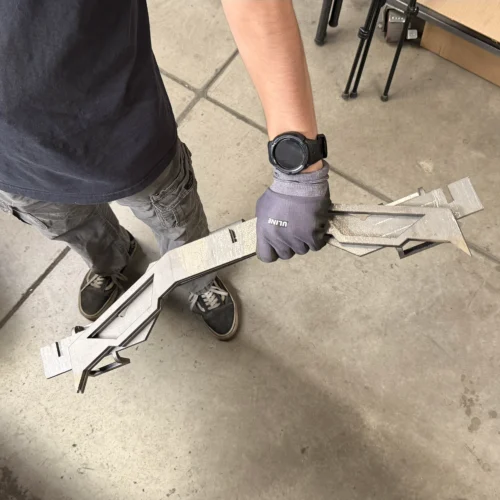 Person in a dark shirt and gloves holding a long, textured metal framework on a concrete workshop floor.