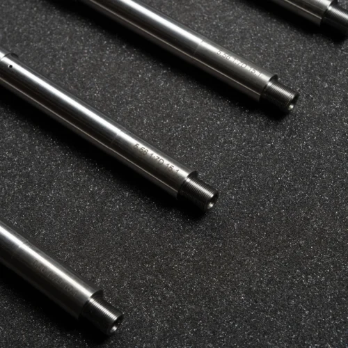 Close-up of stainless steel rods with threaded ends on a dark speckled surface.