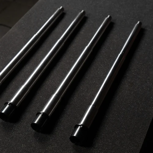 Four slim black and silver cylindrical rods laid diagonally on a dark speckled surface.
