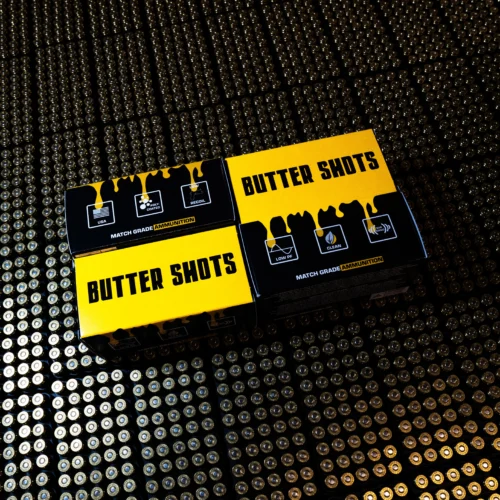 Yellow and black ammunition boxes reading 'BUTTER SHOTS' on a surface covered with rows of bullet casings.