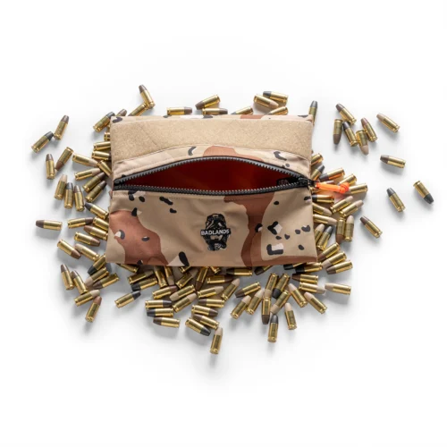Camouflage zip pouch with Badlands logo, open to reveal a red interior, surrounded by scattered brass cartridge casings