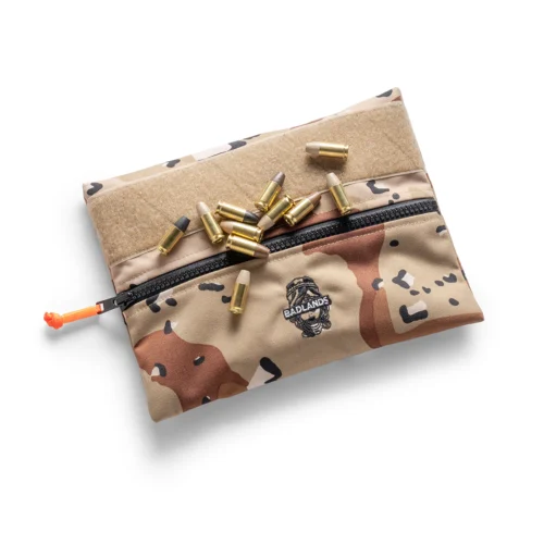 Camouflage zip pouch with orange pull tab, scattered brass cartridge casings, and Badlands logo