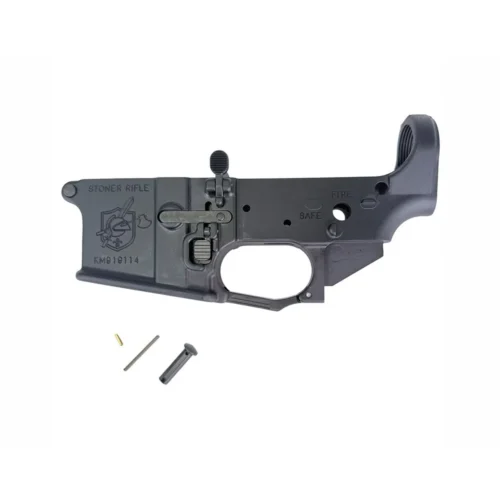 Black AR-style rifle lower receiver with safety markings and trigger guard, with small pins nearby for assembly